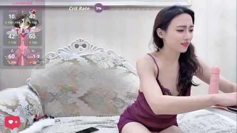 Video of an Asian woman with long black hair, wearing a purple nightgown, sitting on a bed. She holds a pink dildo. Background includes a virtual avatar and a \"CriRate\" overlay.