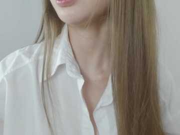 Video of a close-up of a woman's neck and shoulders, wearing a white, slightly unbuttoned shirt with long, straight, light brown hair. The background is plain and light-colored, emphasizing the soft textures of her skin and hair.
