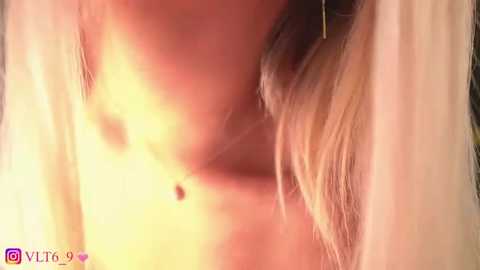 Close-up video of a topless woman with medium-sized breasts, fair skin, and blonde hair, partially obscured by a soft, warm light.