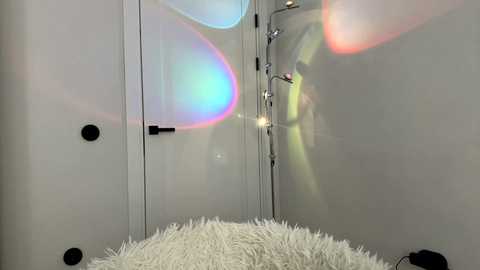 Video of a modern bathroom with a white, textured shower curtain, featuring a colorful, abstract light reflection. The walls are light gray, and a black door is visible on the left. The room is clean and minimalistic.