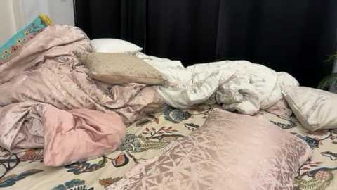 Media: A video shows a messy bed with multiple pillows and a pink and beige comforter, a floral-patterned sheet, and a black curtain in the background.