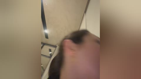 Media: A blurry, close-up video of a person with a dark, bushy beard and long hair, taken indoors with beige walls and a silver towel rack visible.