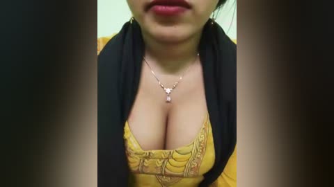 A close-up video of an Asian woman with medium skin tone, wearing a low-cut mustard yellow blouse, black cardigan, and a dainty necklace.