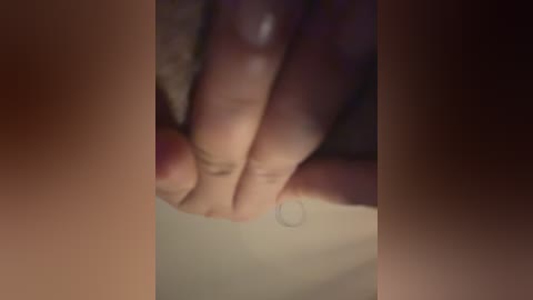 A blurry, close-up video of a hand with light skin, fingering a sheet of paper. The background is dark and indistinct. The image appears to be taken in low light.