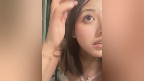 A video of an Asian woman with light skin, straight dark hair, and light makeup, wearing a white lace top, brushing her hair with a hand on her shoulder, partially blurred in the foreground.