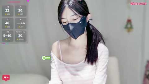 A video of an Asian woman with long black hair, wearing a black mask and white off-shoulder top, indoors, with a \"Welcome\" screen overlay.