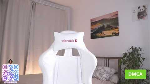 Video of a modern, white gaming chair with \"Razer\" logo, in a minimalist bedroom with a green DMC logo, a potted plant, and a framed landscape painting.