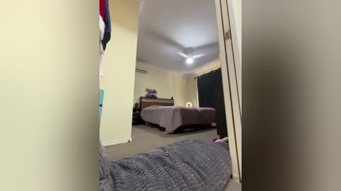 Media: Video of a small, simple bedroom with a bed, a small dresser, and a mirror; beige walls, carpet, and a ceiling fan.