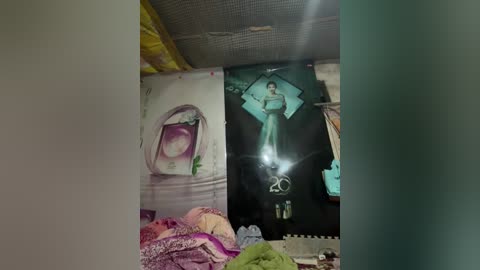 Video of a cluttered room with a large, framed image of a woman in a white veil on the left, a glowing angelic figure in the center, and a green patterned fabric on the right. The walls are beige and the ceiling has a textured finish.