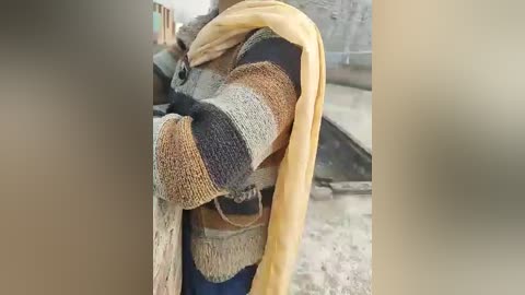 Video of a person wearing a colorful, striped knit sweater with a yellow scarf draped over their shoulders, standing against a blurred, neutral-toned background.
