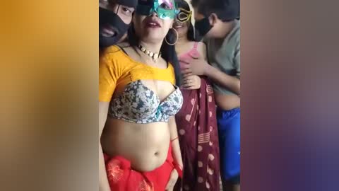 Video of a woman with medium skin tone, wearing a yellow crop top, floral bra, and red skirt, with a mask, surrounded by others in a crowded setting.