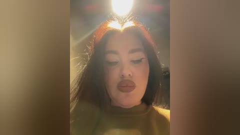 Video of a woman with long, straight brown hair and light skin, wearing a green top, with a bright light shining directly on her face, creating a halo effect.