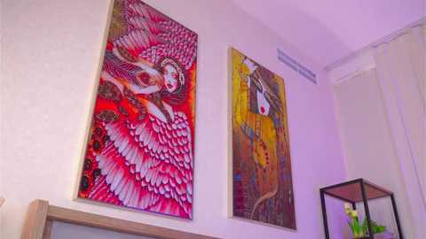 Video of an interior wall with two vibrant, abstract paintings: a large one of a winged woman in red and pink, and a smaller one featuring a stylized face in yellow and orange.