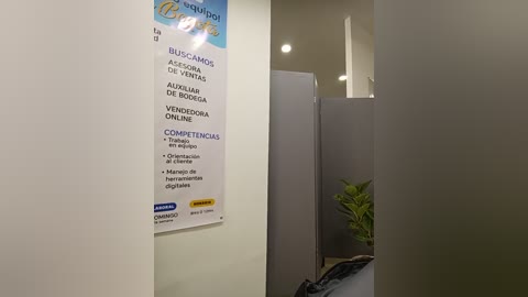Video of a modern, brightly lit hallway with a white wall displaying a blue and white sign in Spanish, advertising \"Buscamos Alimentos,\" featuring bullet points about \"Vender Online,\" \"Compartir Comidas,\" and \"Compartir Ollas.\