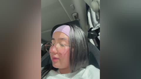 A video of a young woman with long black hair and a purple headband, wearing glasses, sitting in a car. She appears to be in a relaxed state with a slight smile.