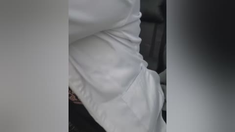 A video showing a close-up of a person wearing a white shirt, partially visible. The shirt is slightly wrinkled, and there is a hint of a black belt in the lower right corner. The background is blurred, with a dark, possibly leather chair.