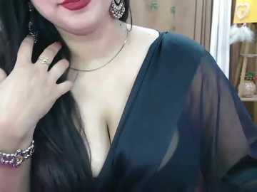 Video of a woman with fair skin, wearing a sheer black top that reveals a deep V-neckline, adorned with large, intricate earrings and a bracelet.