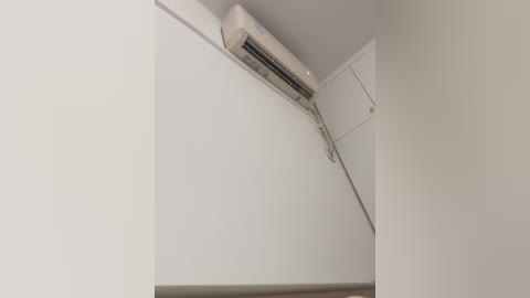A video of a minimalist white room with an air conditioner mounted on the ceiling, set against a smooth, unadorned white wall. The image captures an interior space with a clean, modern aesthetic.