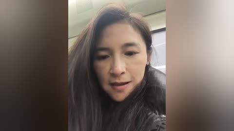 Media: Video of an Asian woman with long, dark hair, wearing a black leather jacket, smiling slightly, taken indoors with blurred background.