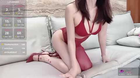 Video of an Asian woman with fair skin, kneeling on a beige couch in red lingerie, with a virtual reality interface overlay displaying health stats.