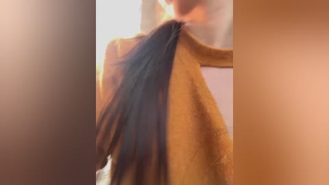A video of a woman with long, dark hair, wearing a mustard-yellow towel, with a blurred background. The image has a warm, soft lighting effect.