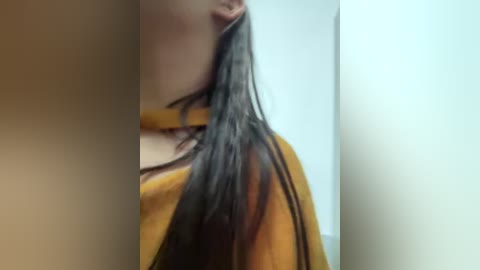 Video of a woman with long, wet, dark hair, wearing a mustard-yellow top, partially obscured by a blurry background, suggesting a bathroom setting.