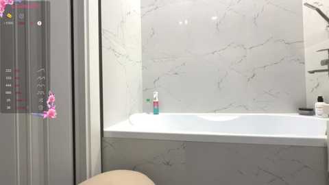 Video of a modern bathroom with a white marble-clad bathtub, a glass shower enclosure, and a pink orchid on the left, featuring a sleek, minimalist design.