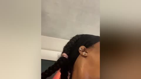 A video of a young Black woman with braided hair and a gold nose ring, captured from a low angle, against a plain white wall.