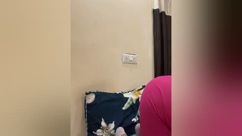 A video of a person's head, blurred, in a room with beige walls, a floral pillow, and a pink shirt partially visible.