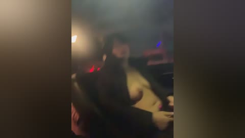 A blurry, dimly lit video shows a person sitting in a dark room with a lit lamp in the background, partially obscured by shadows.