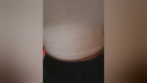 Media: A blurry video shows a person's midsection in a white top and black pants, standing against a beige wall. The image has a soft focus, obscuring details and faces.