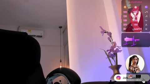 A video of a modern living room with a woman in lingerie on a TV screen, a purple orchid in a vase, and a black couch.