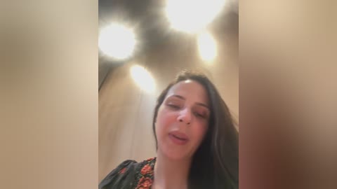 A video captures a young woman with long dark hair and light skin, wearing a black dress with floral accents, smiling with her eyes closed. The background features a dimly lit, arched ceiling with soft, diffused lighting.