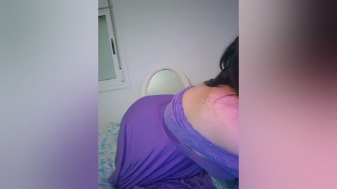 A video shows a woman in purple clothing, lying on a bed, with a mirror and window in the background, capturing a side view of her body.