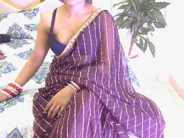 Video of a woman in a purple, striped sari with a blue bra, multiple bangles, and a green leafy plant in the background.