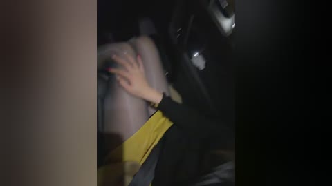 A blurred, dimly lit video captures a person's hand, wearing a yellow and black garment, holding a person's leg, likely in a car, suggesting a tense or intimate moment.