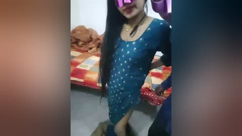 Video of a pregnant woman in a blue, star-patterned dress, standing in a room with a bed and piles of clothes.