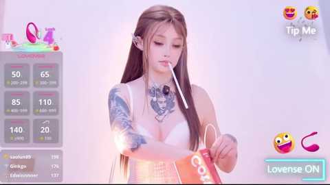 A video of a young woman with long brown hair and tattoos, holding a red and white candy, set against a soft-focus background with game stats and emojis.