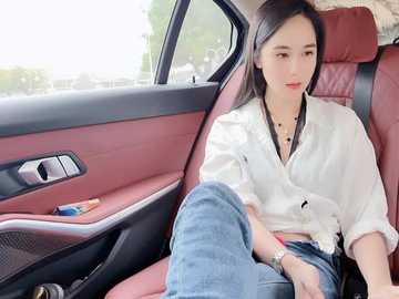 A video of a young Asian woman with straight black hair, wearing a white blouse and blue jeans, sitting in a red leather car seat.