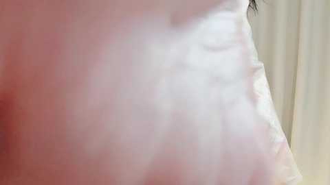 Close-up video of a woman's bare, pale thigh and buttock, showing smooth skin and slight stretch marks, against a blurred beige curtain background.