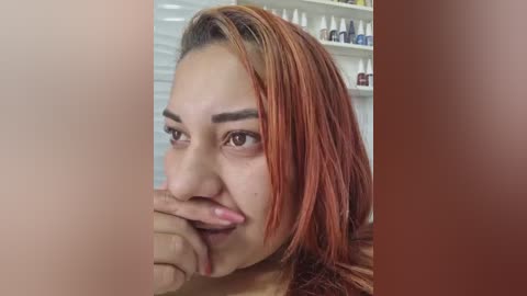 Video of a young woman with reddish-brown hair, light skin, and large brown eyes, biting her fingernails. Background shows a white shelf with bottles of nail polish in various shades.