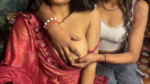 Video of two South Asian women, one wearing a red sari, the other a white lace top, with a hand on the first woman's exposed breast.