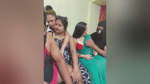 Video of a woman in a black dress holding a young girl in a green sari, both crying. Background shows two other women seated in a room with a red curtain.