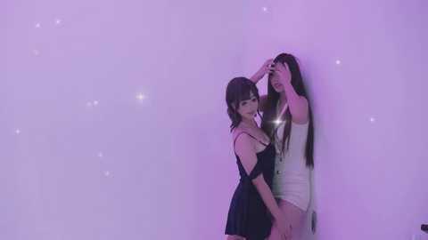 Video of two young Asian women in a smoky, purple-lit room. One wears a black dress, the other a white dress. They appear close, one touching the other's head. Background is hazy, with faint sparkles.