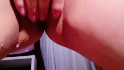 A close-up video shows a hand with manicured nails holding a woman's labia, revealing a reddish hue. The background includes a white curtain and a partially visible mirror.