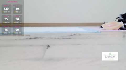 Video of a clean, white-tiled floor with a dark stain in the center. A black backpack and a pink bag rest against a white wall in the background. A weather app shows temperature and weather conditions.