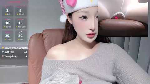 Video of a young Asian woman in a cozy, off-the-shoulder gray sweater, wearing a Santa hat, lying on a brown leather chair in a dimly lit room.