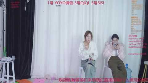 Video of two women in casual attire, sitting on stools behind a white curtain, engaged in conversation, with Chinese text overlaid on the image.