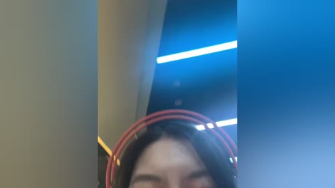 Media: Video of a person with long black hair wearing red headphones, partially obscured by a blue light, with a blurry, dark background.