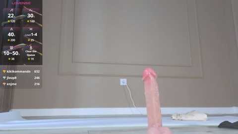 Media: A video depicts a realistic, life-sized, erect pink dildo on a white surface, with a virtual game screen displaying stats and user feedback in the background.